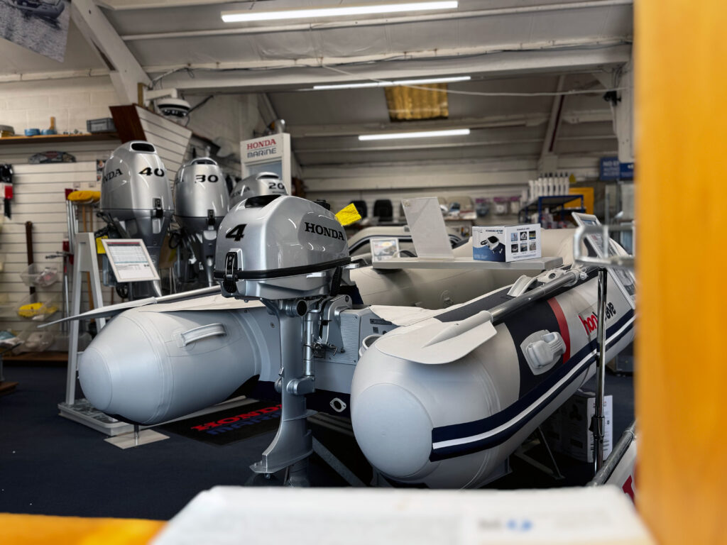 A view of an inflatable boat with a Honda outboard motor displayed in a marina shop. Other outboard motors are visible in the background, with various marine equipment and accessories arranged on shelves.