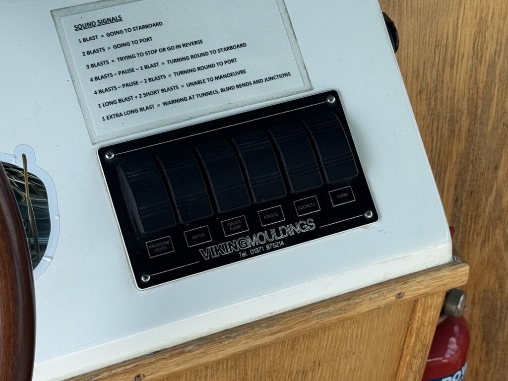 A control panel on a boat featuring labeled push buttons for sound signals, including options for going to port, going to starboard, stopping, and other maneuvering commands. A nearby label lists the meaning of each sound signal.