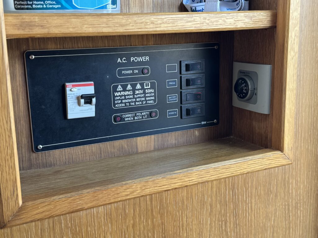 A wooden panel with an electrical control unit. It features a circuit breaker switch, multiple power outlets, and warning labels. To the right, there is a small safe or lockbox embedded in the panel.