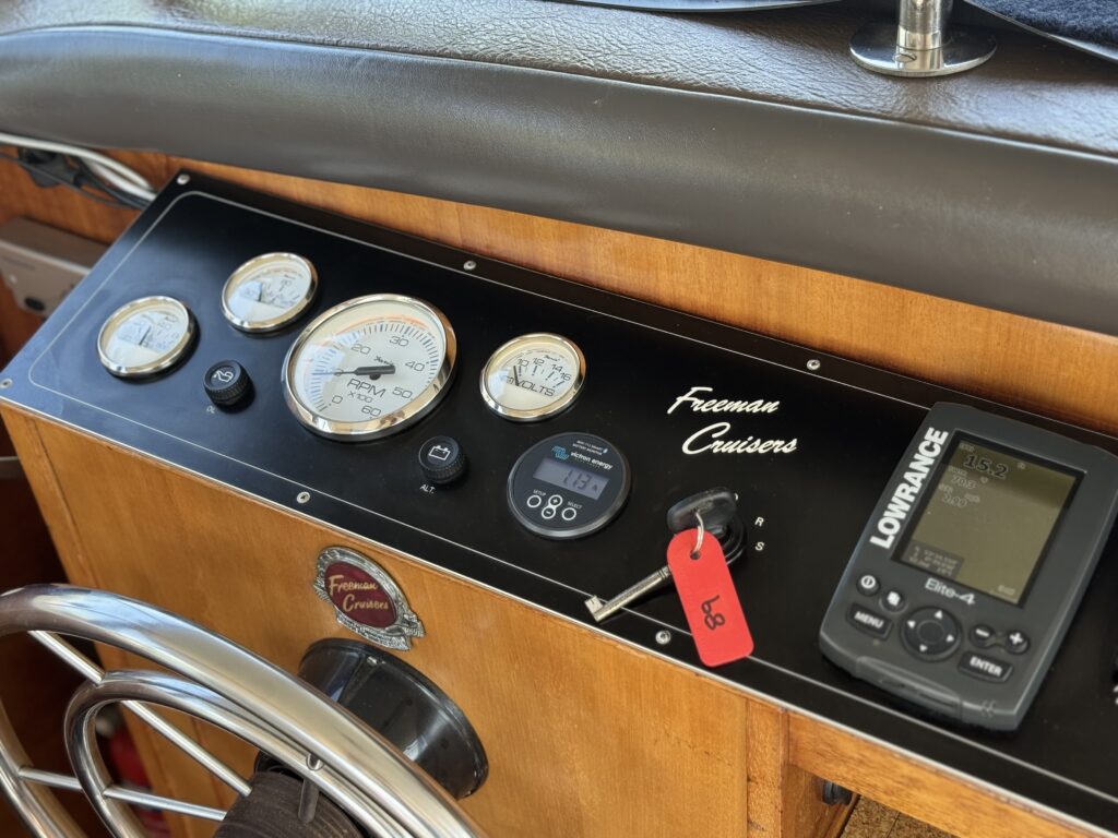 A control panel featuring various gauges and instruments, including speedometer, fuel gauge, and a Lowrance fish finder. The panel has a wooden finish, with the name 'Freeman Cruisers' displayed prominently.