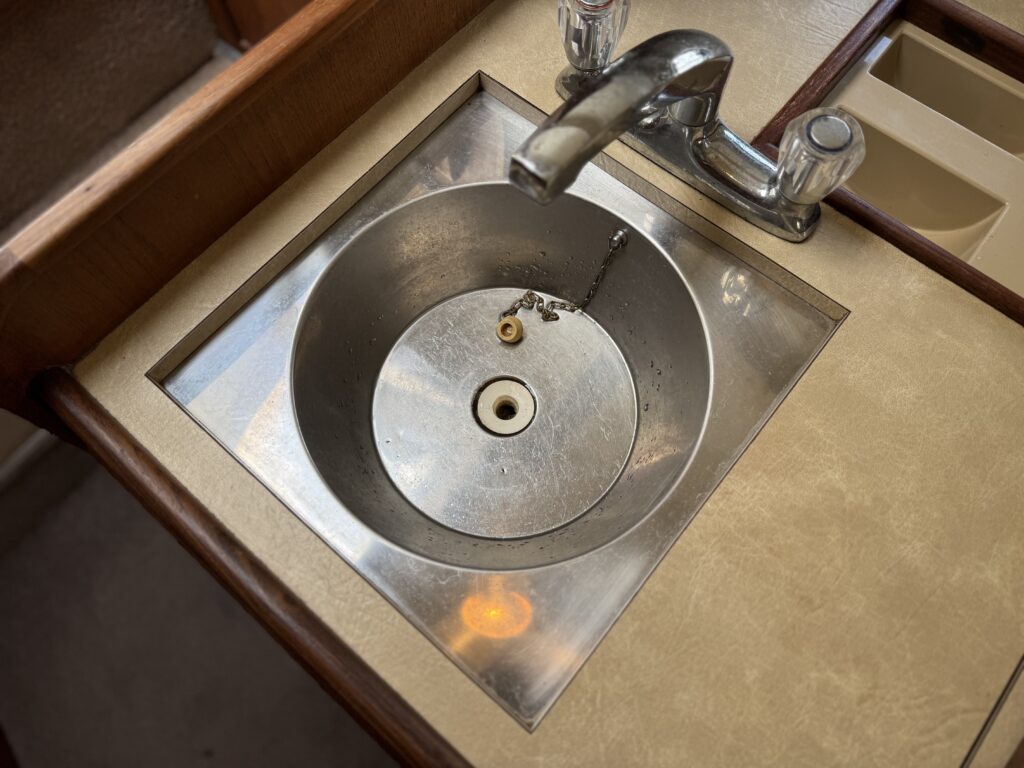 A stainless steel sink with a circular basin and a central drain is installed in a countertop. The faucet is shiny metal with two separate handles on either side.