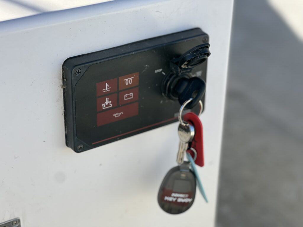 A control panel mounted on a white surface features several buttons labeled with icons and a key slot. A set of keys hangs from the panel, including a key fob with a logo.