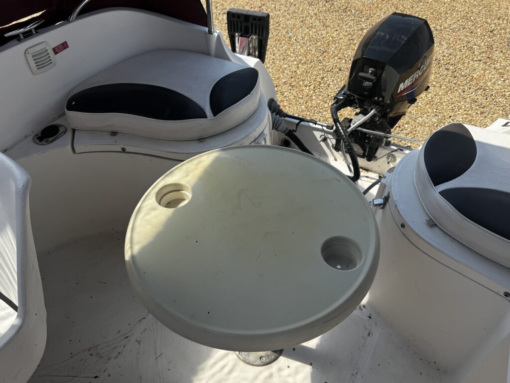 An outdoor seating area on a boat featuring two circular cushioned seats in navy and white, with a central circular table that has two cup holders. A small outboard motor is visible in the background.