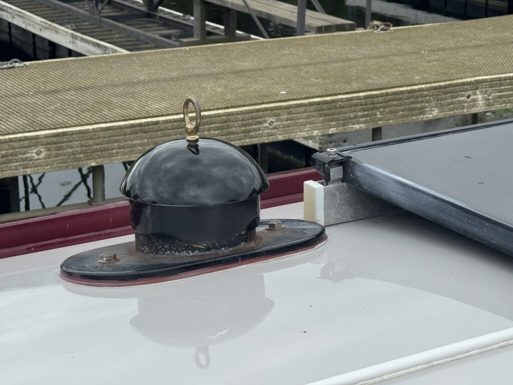 A black metal boat horn mounted on a circular base is shown on the roof of a boat. In the background, a wooden dock and water are visible.