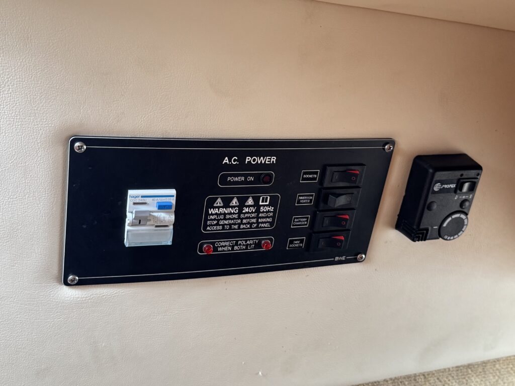 A control panel for A.C. power mounted on a light-colored surface. It features a switch labeled "POWER ON," several indicator lights, and warning labels regarding voltage, along with a small black device on the right side.