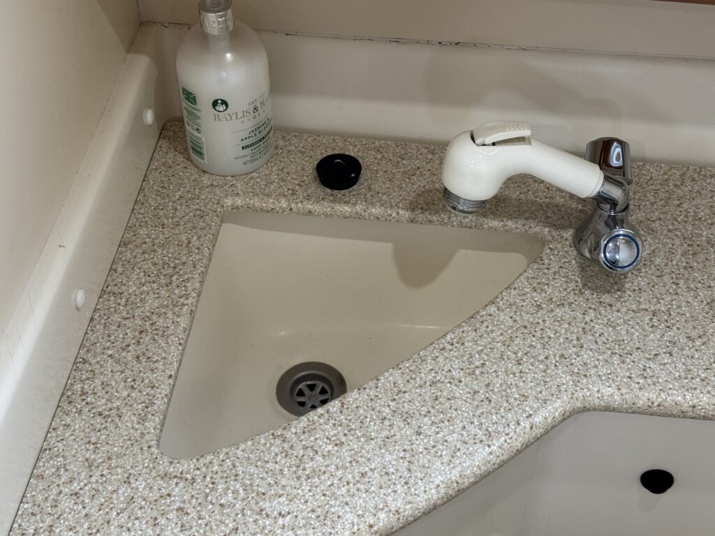 A granite countertop with an integrated triangular sink. The sink features a chrome faucet on the right and a drain at the bottom. There is a bottle of liquid soap on the left side of the countertop and a black cap beside it.