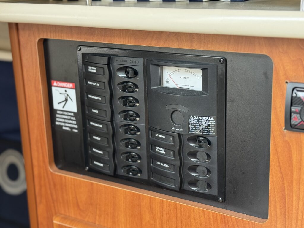 A control panel with multiple switches and a voltmeter mounted on a wooden surface. Warning labels are visible, including one indicating emergency exit procedures and another marked with 'Danger' beside the switches.
