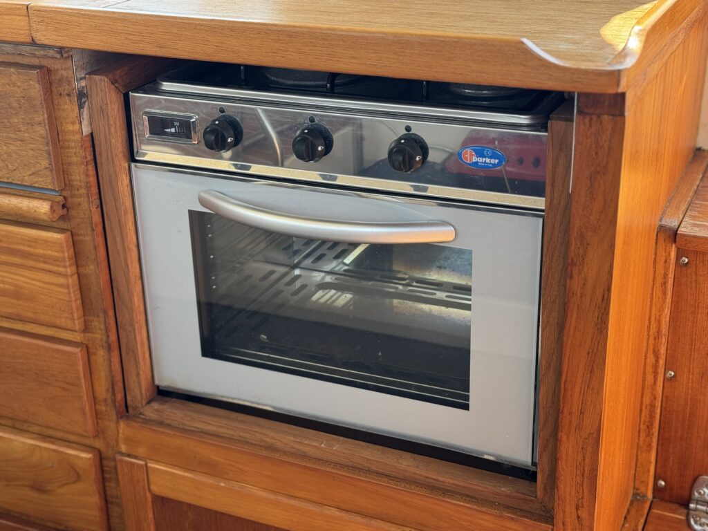 A built-in kitchen oven with a stainless steel front and three control knobs on top. The oven features a glass door that allows visibility of the interior, which has a metal rack inside. The surrounding cabinetry is made of wood.