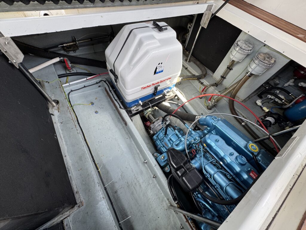An overhead view of a boat's engine compartment showcasing a blue engine with various hoses and wiring. A white fuel tank sits on top, and several transparent fuel filters are visible on the left side against a gray background.