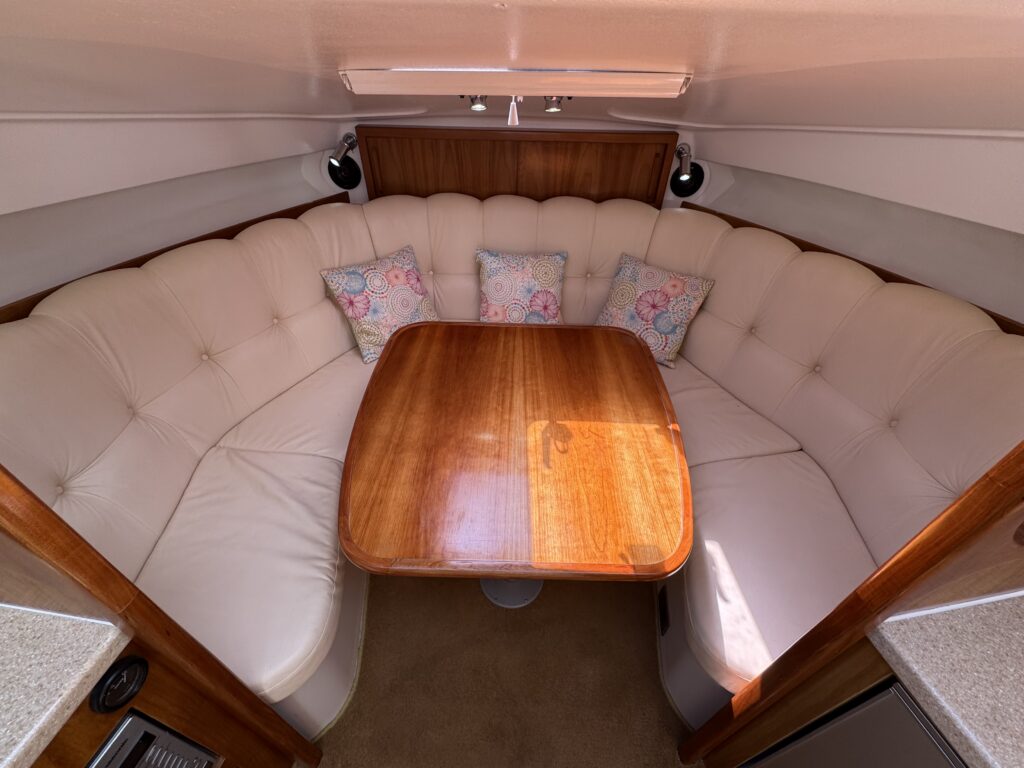 An overhead view of a circular, cream-colored upholstered seating area with a wooden table in the center. The plush seating has decorative pillows with floral patterns, and the surrounding walls are wooden, creating a cozy interior space.