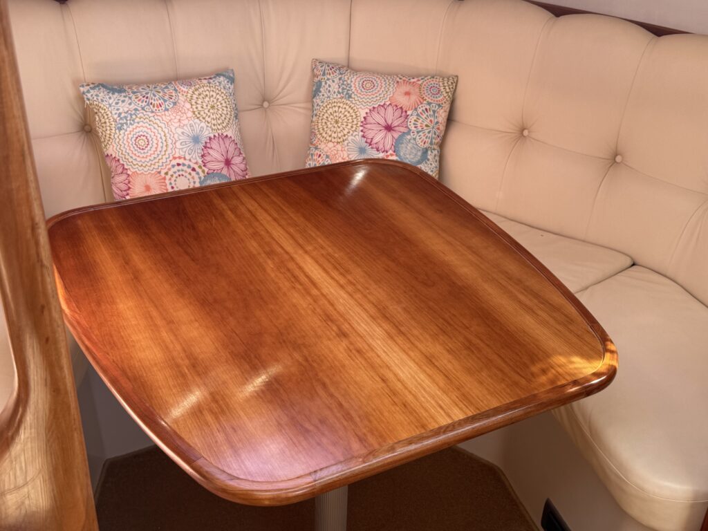A polished wooden table with rounded edges is positioned in a nook. The backrest features beige upholstery with two decorative throw pillows in vibrant floral patterns.
