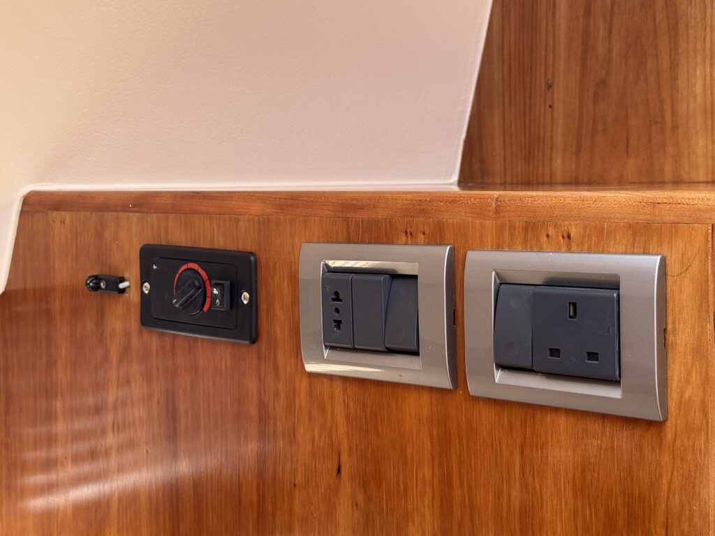 A wooden wall featuring two electrical outlets with metal covers, positioned beside a black switch panel with a red indicator. The outlets include standard US-type plugs.