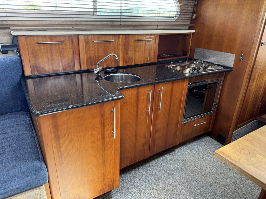 A wooden kitchen area featuring a black granite countertop, a circular sink, a four-burner gas stove, and an oven. The cabinetry above includes three doors, and the space is complemented by gray carpeting and a blue upholstered seating area.