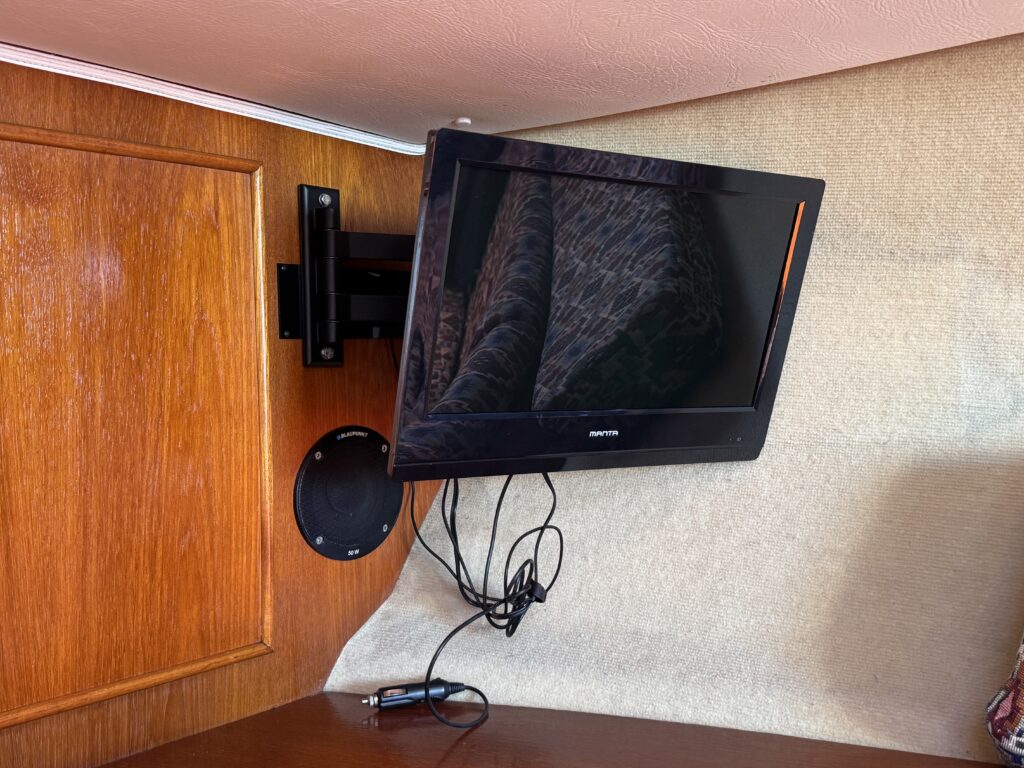 A flat-screen television mounted on a wall with a speaker below it. Visible cables are connected to the TV, and the background features wooden paneling.