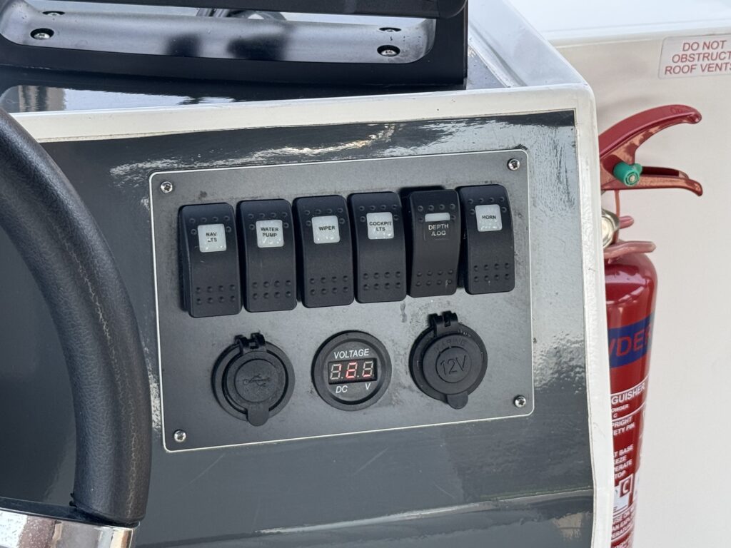 A control panel featuring six switches for various functions, a voltage indicator displaying "8.8," and two round ports labeled for connectivity. A fire extinguisher is positioned to the right, visible in the background.