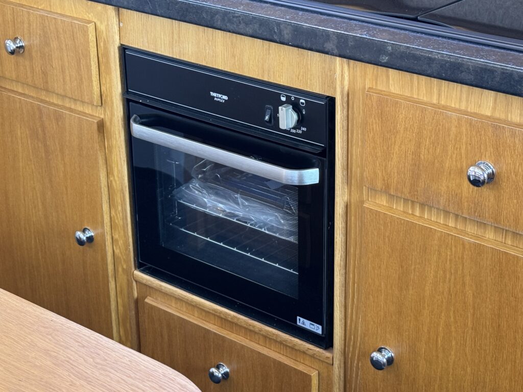 A built-in black oven with a glass door is installed in wooden cabinetry. The oven features a control dial and an electronic display, and it is positioned beneath a counter with a dark countertop.