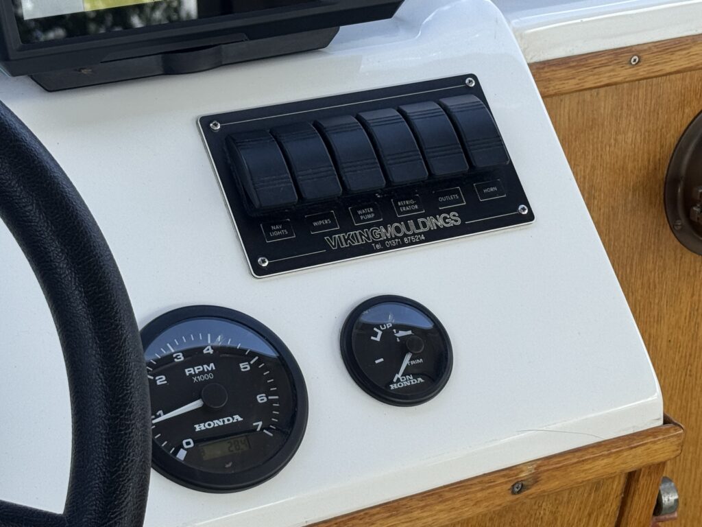 A boat control panel featuring five black push buttons labeled "Viking Mouldings" above gauges. A black RPM gauge with "Honda" on it is shown on the left and an oil pressure gauge on the right, both with white dials and black backgrounds.