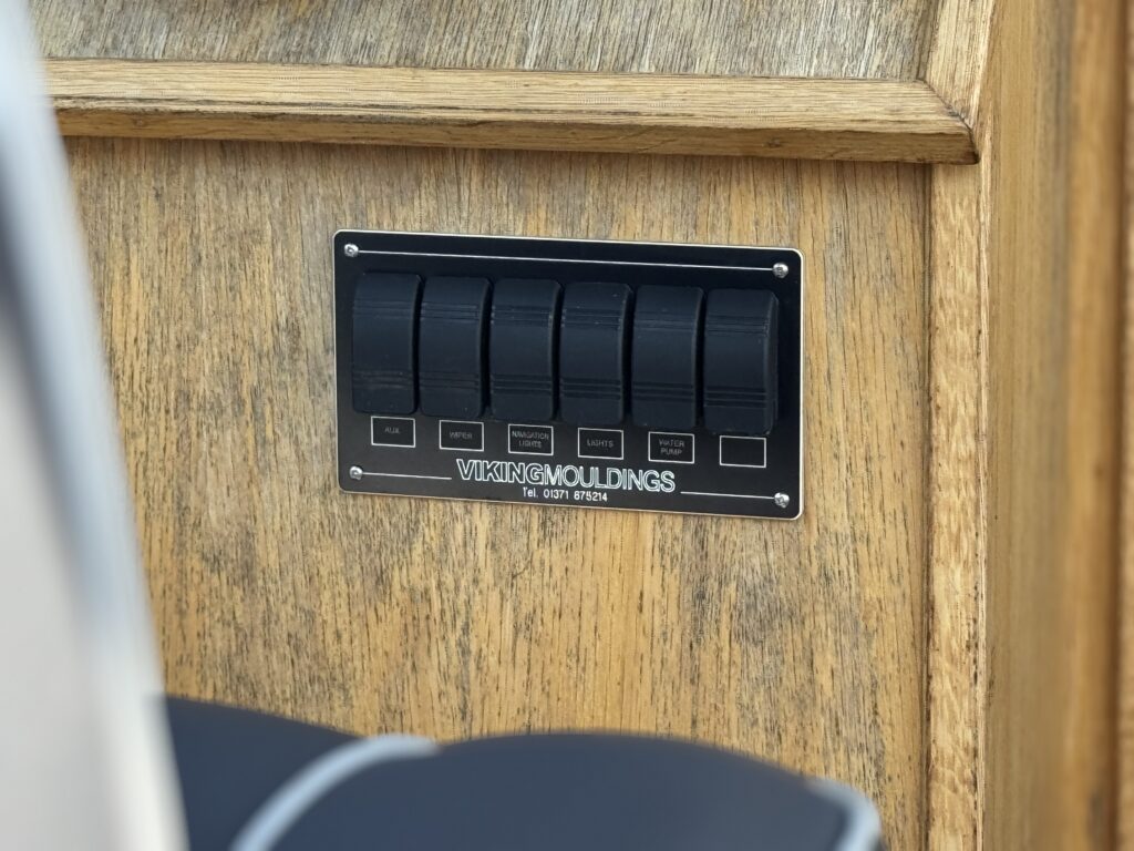 A control panel mounted on a wooden surface features five black switches, each labeled with different functions, such as light and power. The panel has an embossed logo reading 'Viking Mouldings' at the bottom.