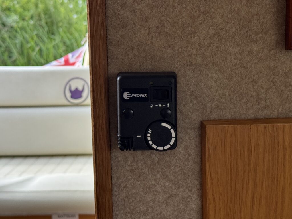 A black control panel mounted on a wall, displaying the brand name "E-propex" and various buttons and a dial. In the background, a cushioned seating area with a light-colored surface is partially visible.