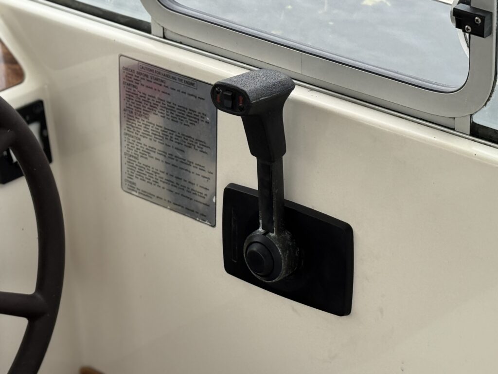A black boat throttle lever is mounted beside a window on a cream-colored console, with a steering wheel partly visible at the left edge.