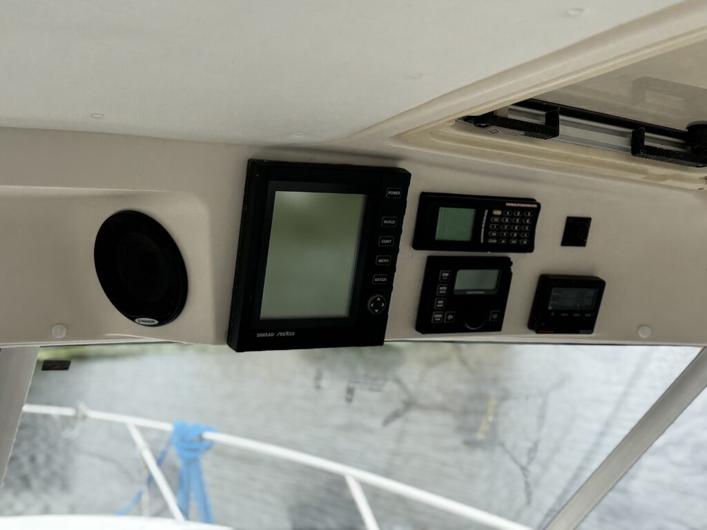 A boat helm panel with navigation screens, radios, and controls above the windshield, with the bow and water visible outside.