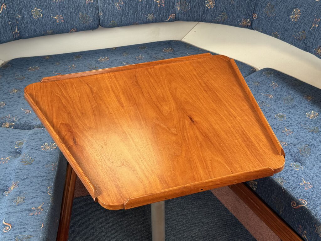 A varnished wooden table sits in a blue upholstered seating area with patterned cushions and a carpeted floor.