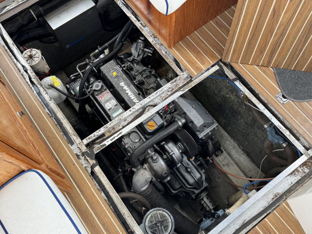 An open boat engine compartment reveals two visible inboard engines beneath removable deck panels, surrounded by teak flooring and white seat cushions.