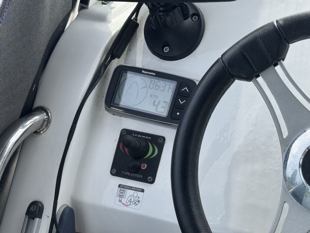 A boat helm with a steering wheel, digital gauge display, and throttle control mounted on a white console.