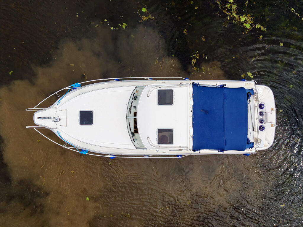 A white Marex 280 Holiday boat seen from above on shallow water, with a blue canopy and ripples around the hull.