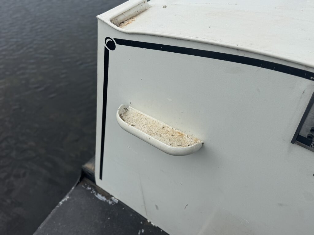 A white narrowboat cabin with a small side handle and black trim, shown beside dark water.