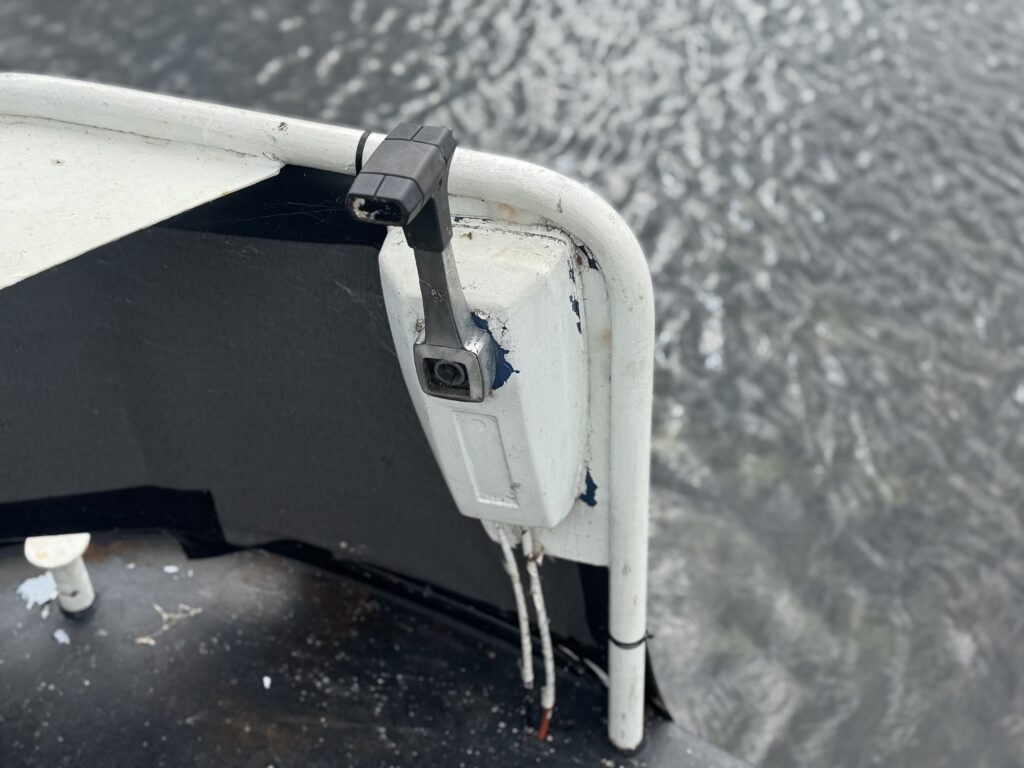 A small white security camera is mounted on the corner of a narrowboat, with rippling water in the background.