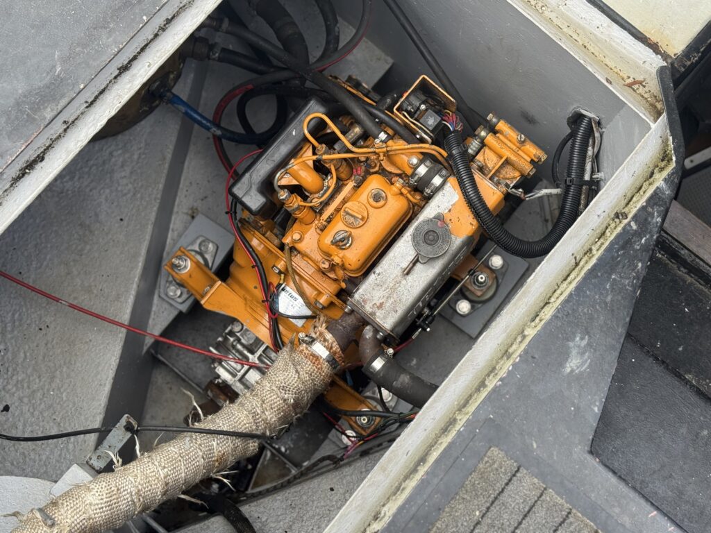 An orange marine engine mounted in a narrow boat engine bay, with black hoses and wiring around it.