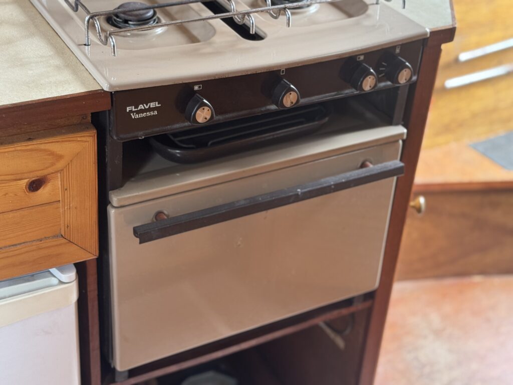 A compact Flavel Vanessa stove with two burners and an oven is built into a narrowboat kitchen beside a wooden cabinet.