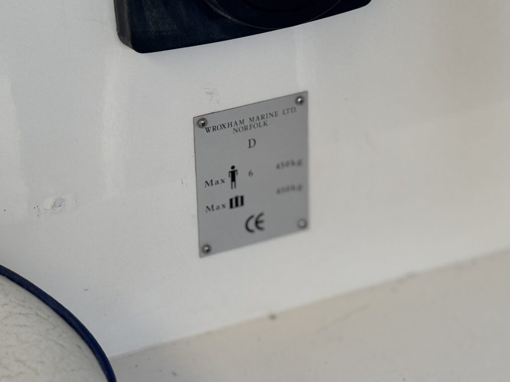 A small metal identification plate on a white surface, labeled with the Sheerline 950 context and mounted beside a blue cable.
