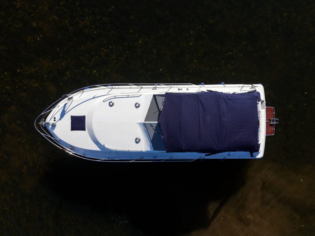 A white motorboat with a covered rear deck is seen from above on dark water.
